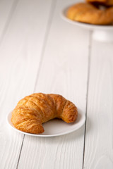 Warm crispy flaky croissant roll on white plate and distressed table.