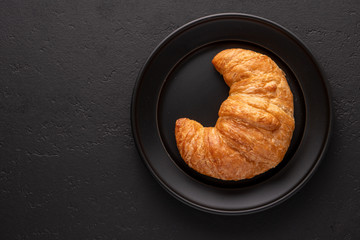 Warm crispy flaky croissant roll on white plate and distressed table.