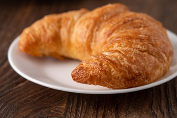 Warm crispy flaky croissant roll on white plate and distressed table.