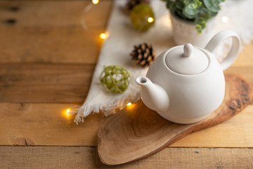 Tea time and tea drinking. White porcelain teapot on a wooden board on a wooden table with a pink garland. View from above