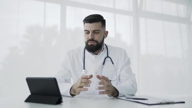 Doctor is looking at camera of pc tablet and talking to patient