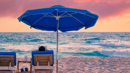 Man reads book by the ocean on Singer Island, Florida beach during a dramatic sunrise