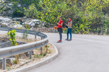 Two male longboarders carrying their longboards in their hands while climbing uphill and preparing for a downhill slide. Wearing red t-shirts, green hat, and super cool sunglasses.