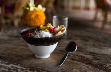smoothie bowl in a coconut shell plate with with strawberries, chia seeds, banana, granola, flower on wooden background