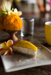 raw vegan cake with cashews and coconut and mango on top on wooden background