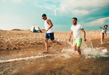 Fototapeta premium Friends running through the water at sunset