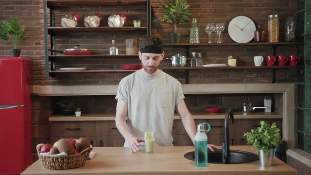 Young attractive handsome Caucasian man after training tastes fresh organic smoothie feels bad and throws up into the sink in kitchen. Healthy food, nutrition, being on a diet. Male portrait, close up