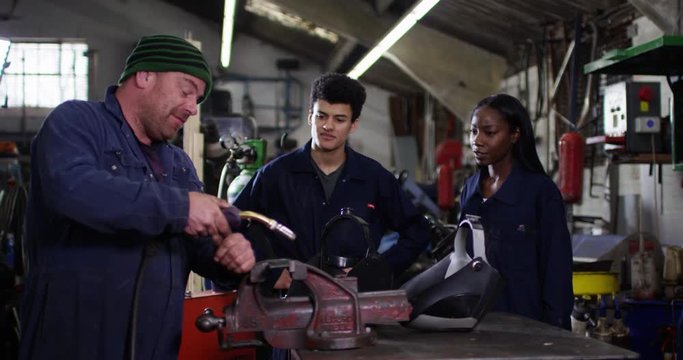 4K Young apprentices learning from experienced mechanic in auto repairs shop. Slow motion.
