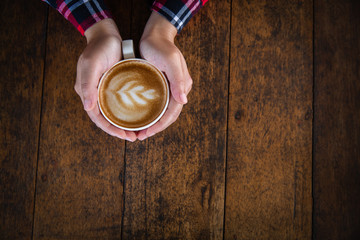 Woman hand holding a cup of coffee on an old wooden table, top view