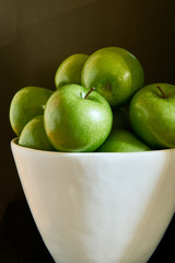 Green Granny Smith cooking apples in a white bowl against a brown background.