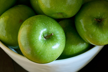 A close-up image of a group of green Granny Smith cooking apples in a white bowl from above.