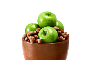 A brown earthenware bowl filled with green Granny Smith apples and brown hazelnuts isolated on white background.
