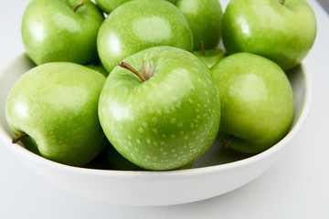 Green Granny Smith cooking apples in a white bowl close-up from above.