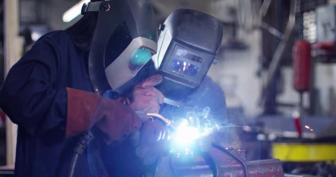 4K Male & female metalworkers welding metal parts in workshop. Slow motion.
