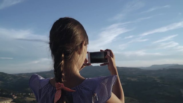Little girl child take photos of mountains by smartphone camera at sunset. San Marino, Italy