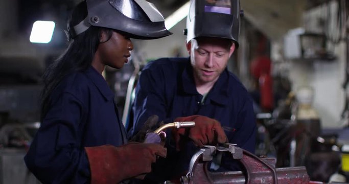 4K Experienced metalworker training young female apprentice in industrial workshop. Slow motion.