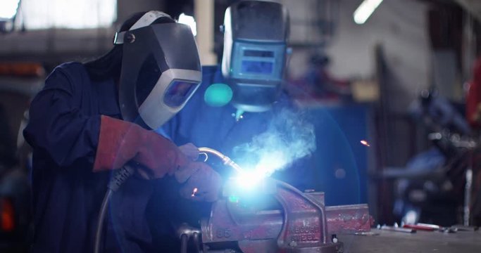 4K Male & female mechanics welding metal parts in workshop & smiling. Slow motion.