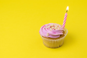 Cupcakes with berry cream and a candle on a yellow background. The concept of the birthday celebration.