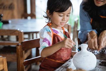 mother and daughter painting ceramic pot in pottery workshop
