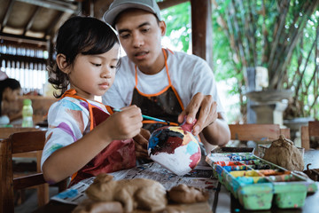 dad and daughter painting ceramic pot in pottery workshop together