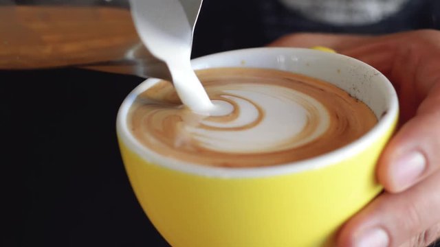 A skillful barista pouring a rosetta pattern latte art in a yellow coffee cup | Gourmet Coffee House | Shot in HD at cinematic 24 fps