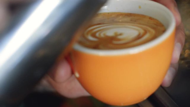 A skillful barista pouring a rosetta pattern latte art, with steamed milk, in an orange coffee cup | Gourmet Coffee House | Shot in HD at cinematic 24 fps