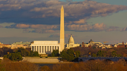 Washington DC panorama with famous landmarks during cloudy winter sunset. Lincoln Memorial, Washington monuments and United States Capitol in city skyline.