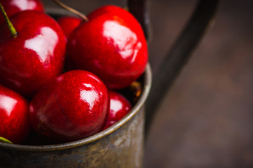 Ripe and juicy cherries in old metal cup on the dark rustic background. Selective focus. Shallow depth of field.