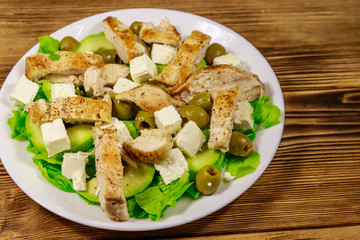 Tasty salad with fried chicken breast, green olives, feta cheese, avocado, lettuce and olive oil on wooden table