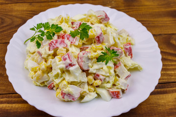Salad with crab sticks, sweet corn, chinese cabbage, eggs and mayonnaise on wooden table