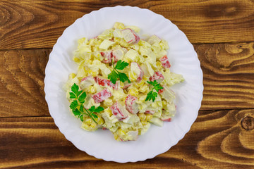 Salad with crab sticks, sweet corn, chinese cabbage, eggs and mayonnaise on wooden table
