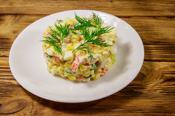 Salad with crab sticks, sweet corn, cucumber, eggs and mayonnaise on wooden table