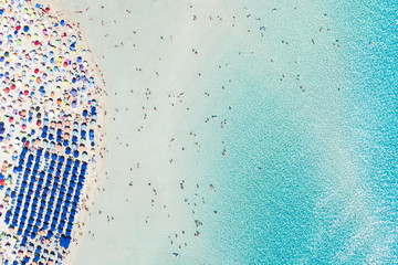 Stunning aerial view of the Spiaggia Della Pelosa (Pelosa Beach) full of colored beach umbrellas and people sunbathing and swimming in a beautiful turquoise clear water. Stintino, Sardinia, Italy.