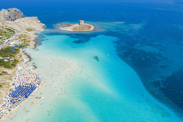Atemberaubende Luftaufnahme des Spiaggia Della Pelosa (Pelosa Beach) voller farbiger Sonnenschirme und Menschen, die sich in einem wunderschönen türkisfarbenen klaren Wasser sonnen und schwimmen. Stintino, Sardinien, Italien.