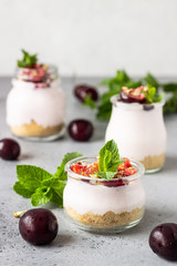 No baked cheesecake with cherry in glass jars, fresh cherries and mint on a grey stone background. Healthy dessert. Copy space.