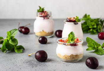 No baked cheesecake with cherry in glass jars, fresh cherries and mint on a grey stone background. Healthy dessert. Copy space.