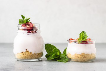 No baked cheesecake with cherry in glass jars, fresh cherries and mint on a grey stone background. Healthy dessert. Copy space.