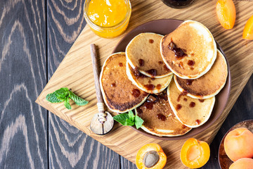 American pancakes or fritters with jam, fresh apricot and mint. Delicious dessert for breakfast. Wooden background, rustic style.  