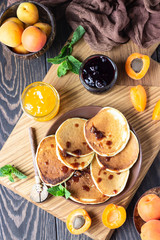 American pancakes or fritters with jam, fresh apricot and mint. Delicious dessert for breakfast. Wooden background, rustic style.  
