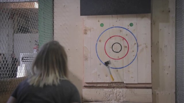 Slow motion footage of a girl throwing an axe at a target.
