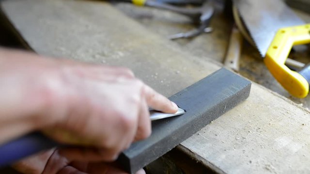 Carpenter sharpening a chisel in a small workshop, focus on the index finger.