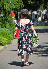 Old woman is walking in the cemetery with a bunch of flower