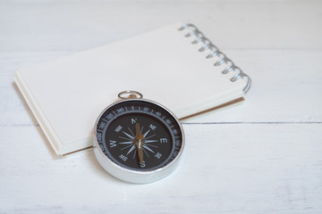 Compass and brown notebook on white wooden table background, journey planning concept