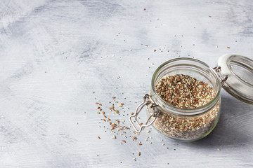 Cereal mixture for healthy keto crackers of chia seeds, flax, sesame, ground pumpkin seeds in a glass jar on a gray wooden background, horizontal