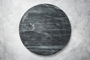 Round slab of black marble on a grey textured background.