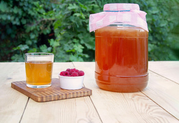 Glass jar with Kombucha, poured glass with Kombucha and raspberries in the summer garden.