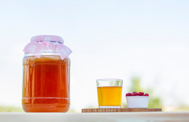 Kombucha  in a jar on a light wooden table against the sky, a glass filled with Kombucha   with raspberries.