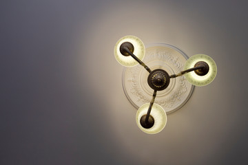 View from below on a retro style ornate metal chandelier with three lamps hanging from a ceiling in...