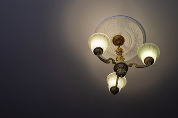 View from below on a retro style ornate metal chandelier with three lamps hanging from a ceiling in a room.