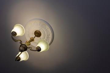 View from below on a retro style ornate metal chandelier with three lamps hanging from a ceiling in...
